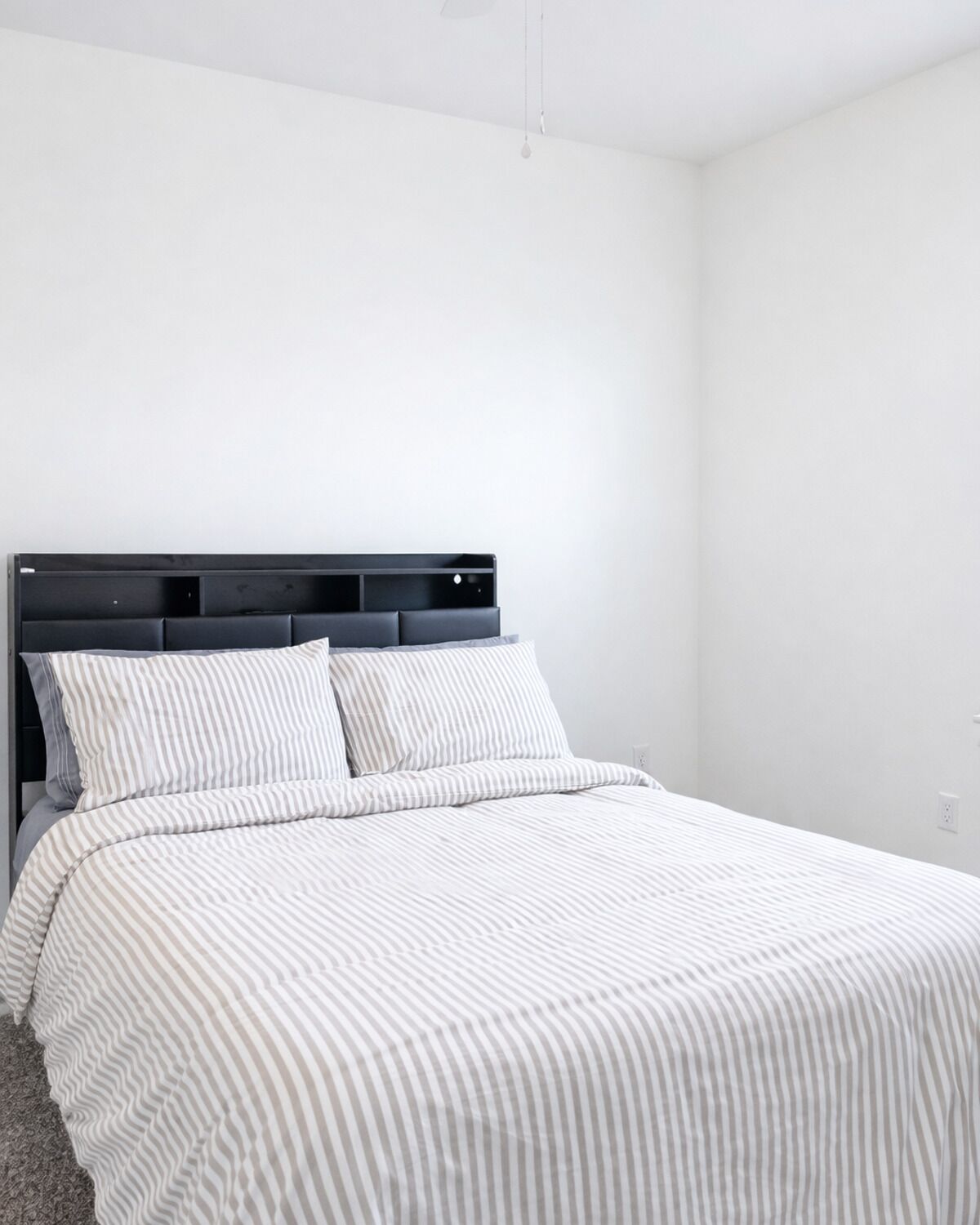 Een slaapkamer met een bed, hoofdeinde en een effen muur.