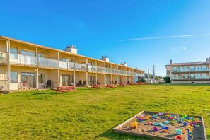 A hotel with multiple balconies, a grassy lawn, and a children's play area with toys.