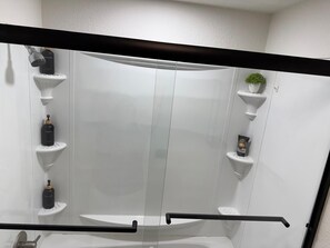 A modern bathroom with a glass shower enclosure, white fixtures, and a small potted plant.