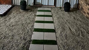 A gated outdoor area with a gravel path, two potted plants, and a brick wall.