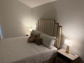 A neatly made bed with a quilted cover, two bedside lamps, and a wooden nightstand.