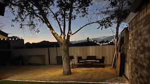 A backyard with a tree, outdoor furniture, and string lights.