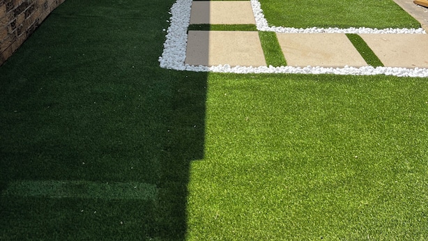 A narrow courtyard with artificial grass, a brick wall, and a metal gate.