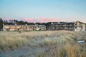 A two-story building with a flat roof and multiple balconies, surrounded by tall grass and trees.