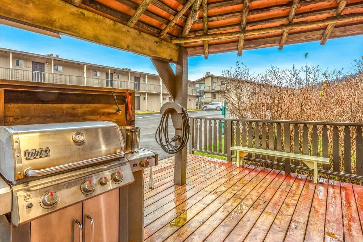 Area barbecue esterna con un pontile in legno, una panchina e vista su un edificio sullo sfondo.
