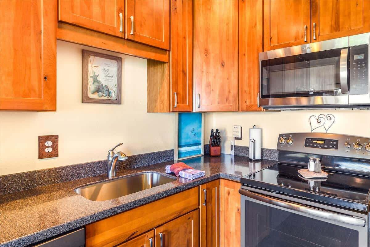 A kitchen with wooden cabinets, a stainless steel sink, a microwave, and an oven.