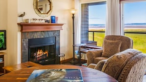 A room with a fireplace, a round table, a sofa, and a view of the outdoors. - Hi-Tide Resort, Top Floor, Queen Bed, Unit 29 (Moclips)