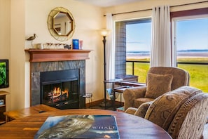 A room with a fireplace, a round table, a sofa, and a view of the outdoors.