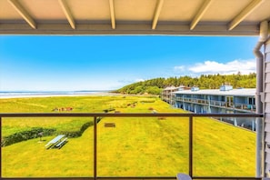 A balcony with a view of a grassy area, a building with multiple windows, and a clear sky.