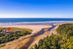 A coastal landscape with a beach, forested area, and a building complex with multiple structures.