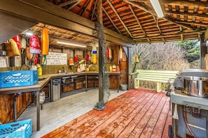 A rustic kitchen with wooden beams, hanging seafood, and a wooden deck.