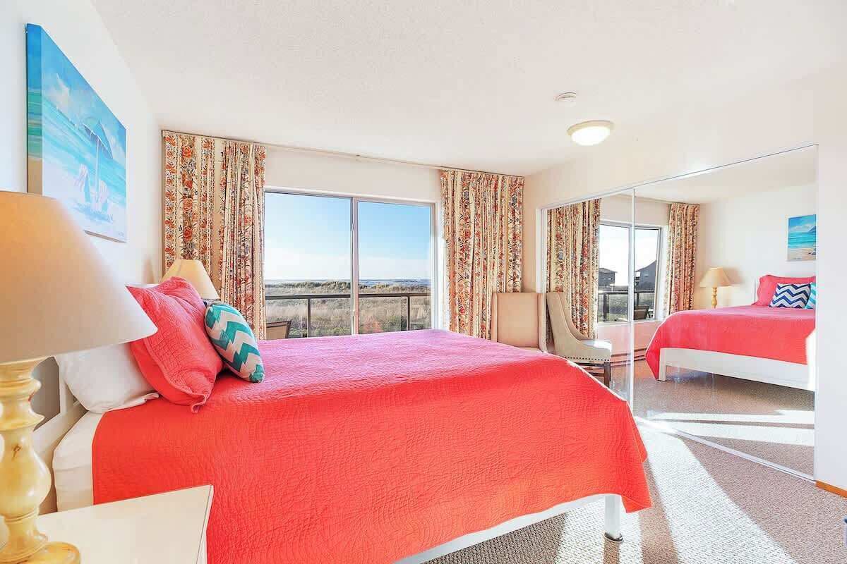 A hotel room with a large bed, a chair, a desk, a mirror, and a view of the outdoors.