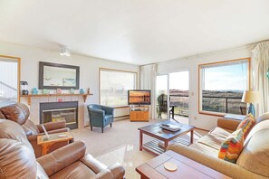 Una sala de estar con sofás de cuero, una chimenea, un televisor y ventanas grandes con cortinas.