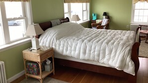 A bedroom with a large bed, two bedside tables, a chair, and a window with a view of a car. - Ocean Front cape cod style home with panoramic views of North Beach. (Hampton)