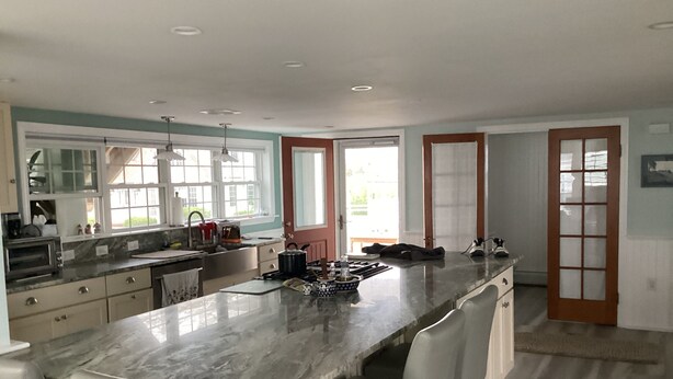 A modern kitchen with a marble island, white chairs, and a large window. - Ocean Front cape cod style home with panoramic views of North Beach. (Hampton)