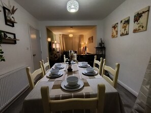 En spisestue med et bord dækket til seks personer, stole, en lysekrone og billeder på væggene.