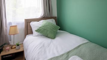 Ein Schlafzimmer mit einem Bett, einem Nachttisch, einer Lampe, einer Pflanze und einem an der Wand befestigten Regal.