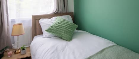 Un dormitorio con una cama, una mesita de noche, una lámpara, una planta y una estantería en la pared.