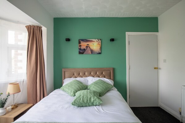 Un dormitorio con una cama, un cuadro, una puerta y una ventana con cortinas.