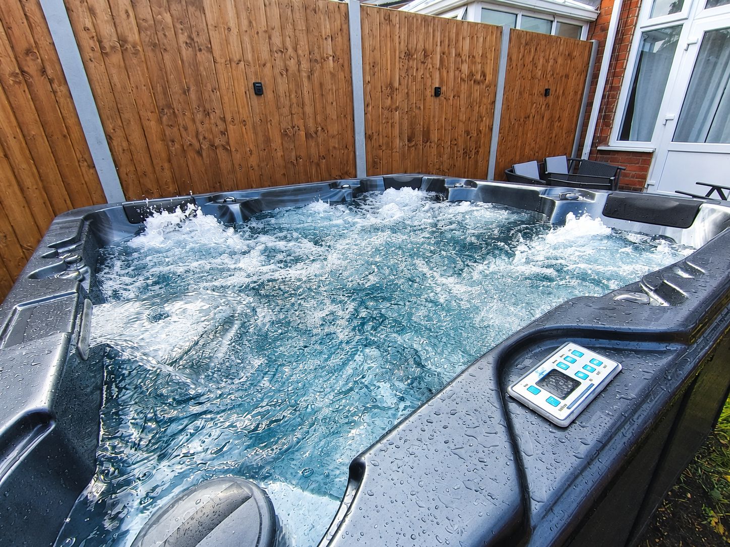 A hot tub with a control panel, surrounded by a wooden fence and a patio area.