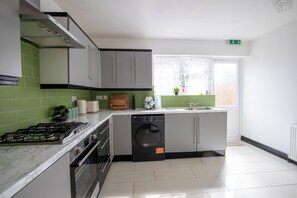 A modern kitchen with a gas stove, dishwasher, and a window with a view. - Hot Tub Retreat | Stylish 3BR Home Near NEC & Airport | Sleeps 6 (Solihull)