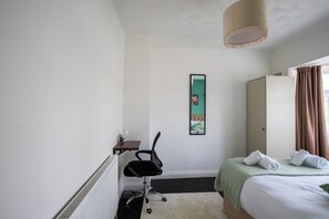 Ein Hotelzimmer mit Bett, Schreibtisch mit Stuhl, Heizkörper, Spiegel und einem Fenster mit Vorhängen.