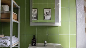 A bathroom with green tiles, a white sink, a mirror, and a shelf with towels. - Stylish 3BR Home Near NEC & Airport | Sleeps 6-7 (Solihull)