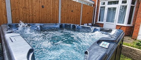 Un jacuzzi en un patio trasero con valla de madera y una casa al fondo.