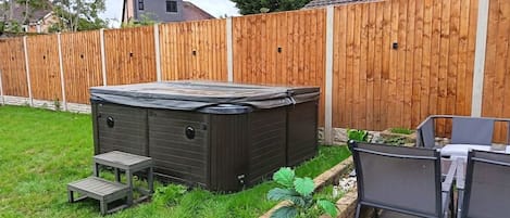 A backyard with a hot tub, a small table, and a chair.