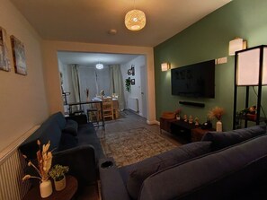 En stue med sofa, fjernsyn og spiseområde med bord og stole.