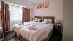 A hotel room with a large bed, two bedside tables, a window with curtains, and a wall with three framed pictures. - Stylish 3BR Home Near NEC & Airport | Sleeps 6-7 (Solihull)