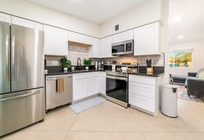 Una cocina moderna con electrodomésticos de acero inoxidable, armarios blancos y un pequeño jardín de hierbas aromáticas.