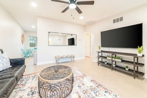 A living room with a sofa, a round coffee table, a TV on a stand, and a ceiling fan.