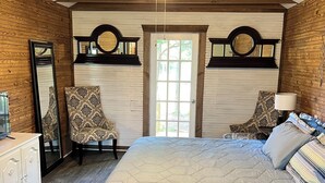 A bedroom with a bed, two chairs, a dresser, a ceiling fan, and a door with a view. - Cozy 1-bedroom cottage in lovely Rocky Mount with AC (Rocky Mount)