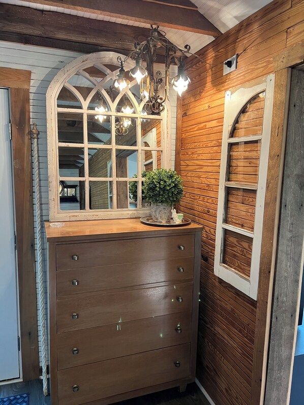 A wooden dresser with drawers, a mirror with a decorative frame, and a chandelier.