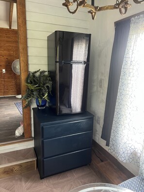 A black refrigerator on a wooden cabinet, a potted plant, and a patterned wall.