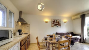A kitchen with a microwave, stove, and a dining area with a table and chairs. - Fiori d'Alivi - PORTO VECCHIO (PORTO VECCHIO)