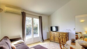 A living room with a sofa, a television on a wooden cabinet, and a dining area with a table and chairs. - Fiori d'Alivi - PORTO VECCHIO (PORTO VECCHIO)