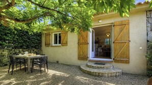 A rustic building with a stone wall, a wooden table with chairs, and a door leading to a kitchen area. - Fiori d'Alivi - PORTO VECCHIO (PORTO VECCHIO)