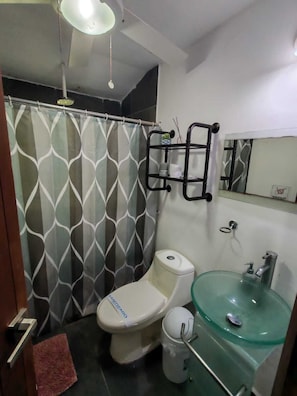 Un baño con inodoro, lavamanos de vidrio, cortina de ducha y toallero.
