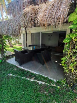 Un área de estar al aire libre con techo de paja, una mesa de vidrio y sillas de mimbre.