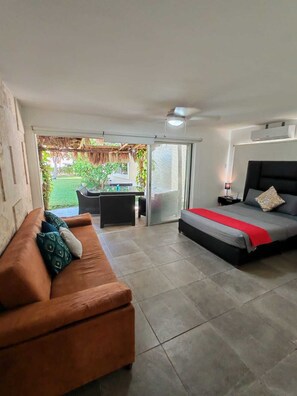 Un dormitorio con cama, sofá, una mesita y vistas a un jardín a través de un ventanal.
