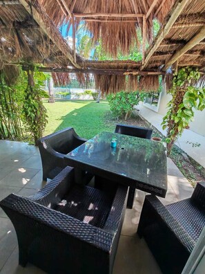 Un patio al aire libre con techo de paja, muebles de mimbre y una pequeña mesa con un objeto azul encima.