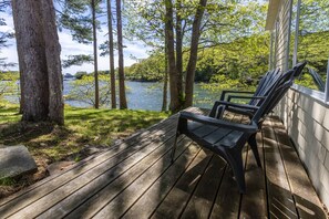 A wooden deck with two chairs overlooking a lake, surrounded by trees.