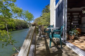 A wooden deck with a table and chairs, overlooking a river and surrounded by trees.
