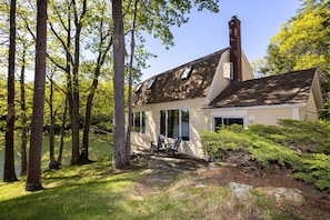 A cabin with a chimney, large windows, and a porch with chairs. - New! Cute boathouse set right on the water (Boothbay)