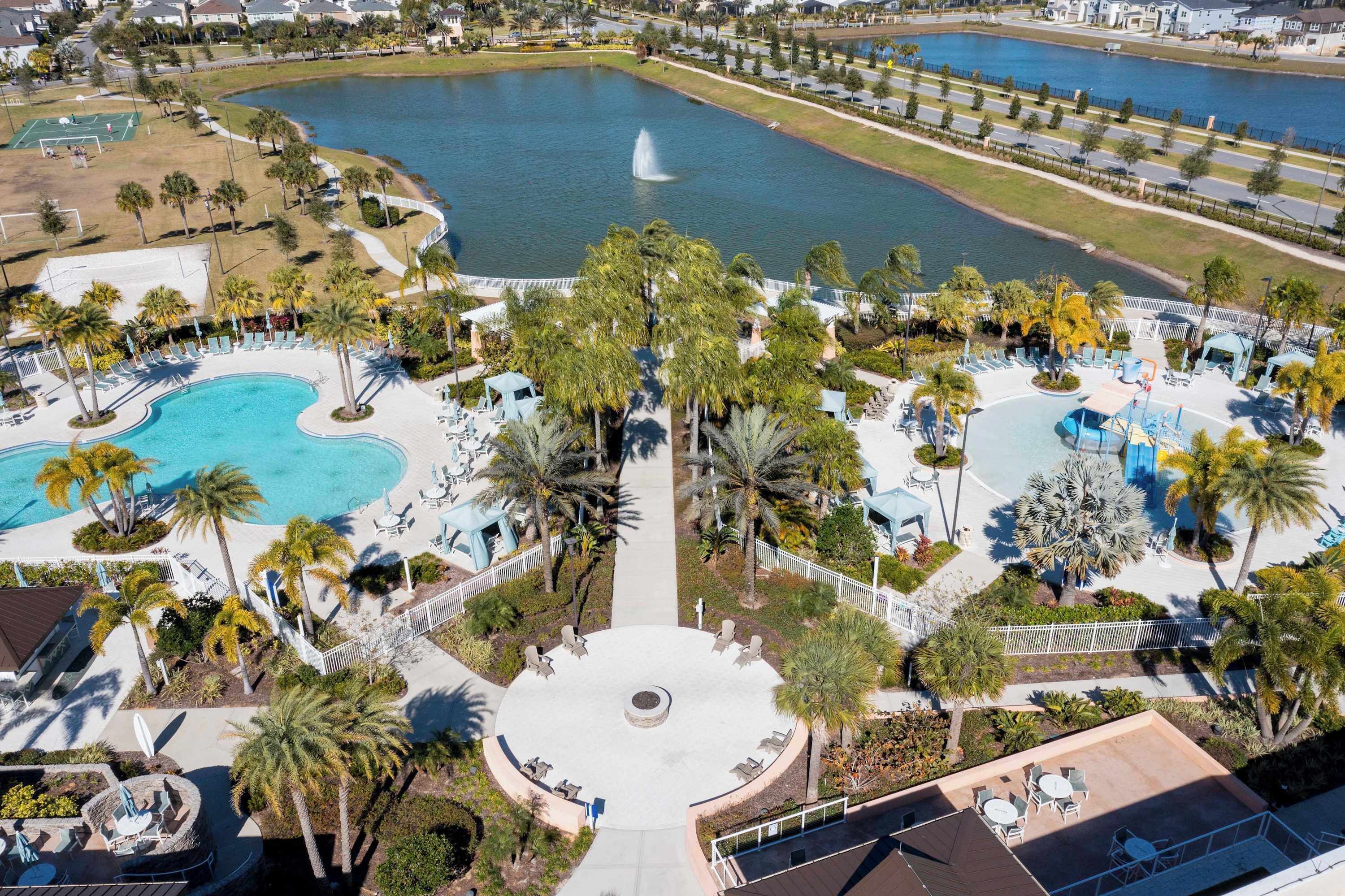 An aerial view of a resort with multiple swimming pools, palm trees, and a central plaza with seating.