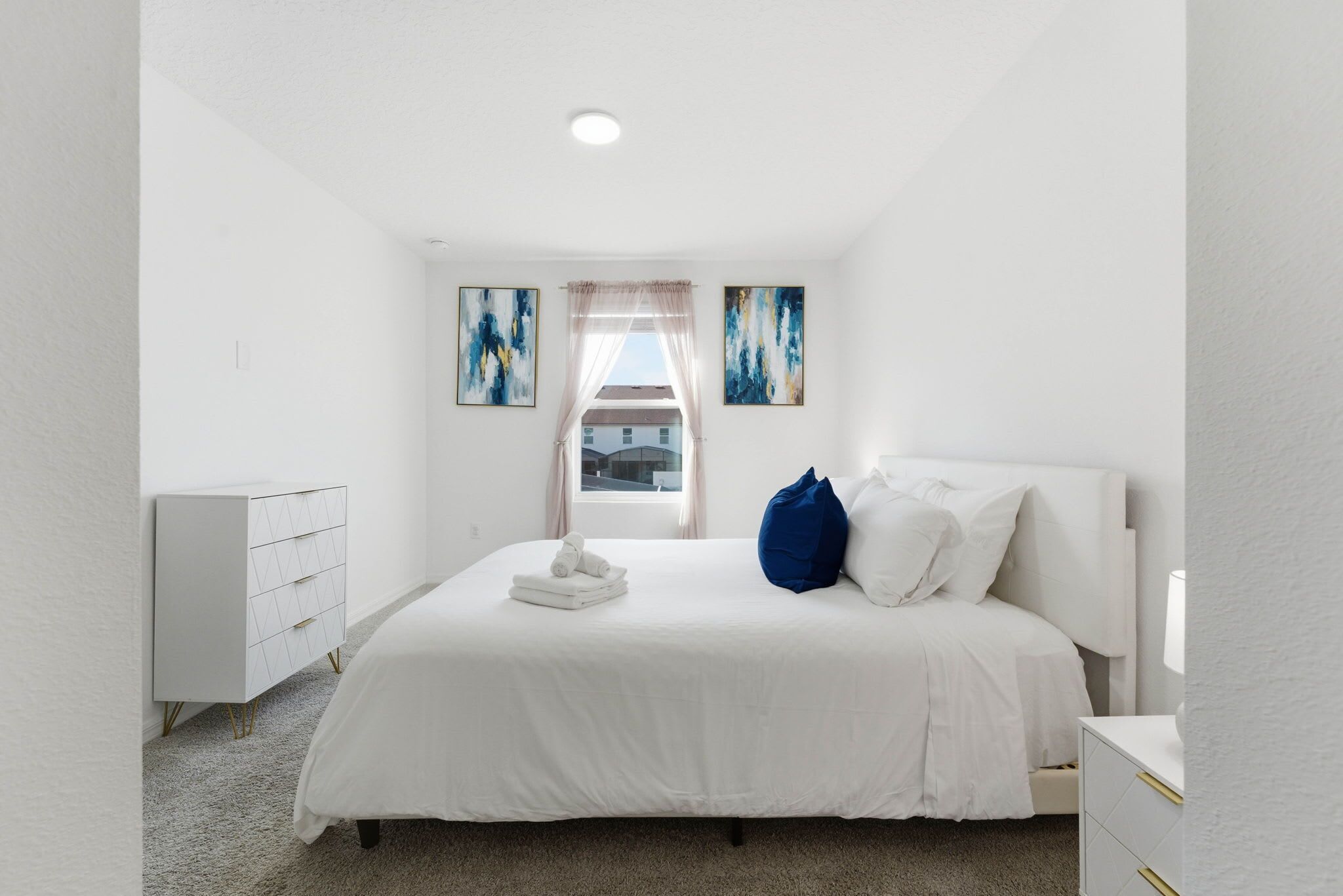 Una habitación de hotel moderna con una cama grande, una mesita de noche, un aparador y dos cuadros abstractos en la pared.
