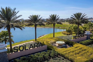 A resort with a sign reading 'SOLARA,' palm trees, a body of water, and a well-maintained lawn. - Family Friendly Stay in Prime Location (Kissimmee)