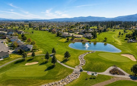 A golf course with a pond, houses, and mountains in the background.. Modern Loft Private Golf Course Retreat